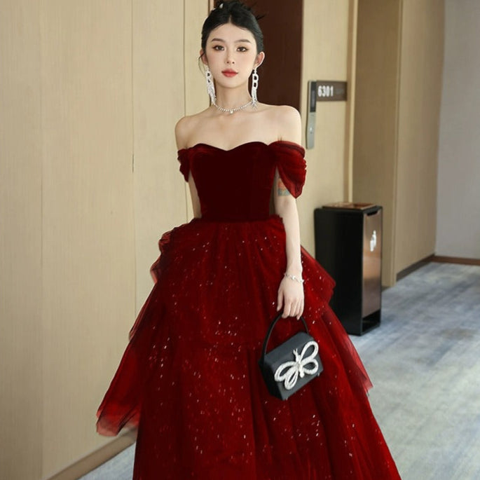 Frau in elegantem, schulterfreiem roten Abendkleid mit Tüllrock und funkelnden Details, hält schwarze Handtasche. Luxuriöse Abendmode, glamouröses Design.