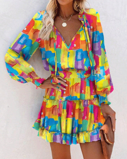 Frau in buntem, abstraktem Kleid mit langen Ärmeln und V-Ausschnitt, hält eine braune Clutch. Sommermode, farbenfrohes Design, trendiges Outfit.