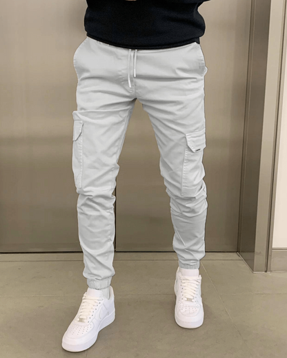 Weiße Cargo-Jogginghose mit Taschen, kombiniert mit weißen Sneakers. Moderne Herrenmode, lässiger Streetwear-Stil, ideal für Freizeit und Alltag.