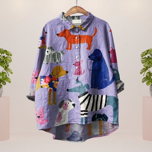 Buntes Damenhemd mit Hundemotiven auf lila Hintergrund, hängend auf einem Kleiderbügel. Modisches Design, ideal für Tierliebhaber.