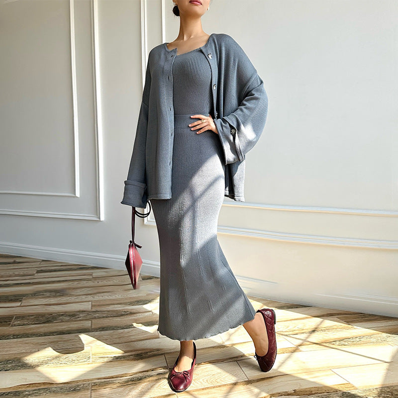 Elegante Frau in grauem Strickkleid und Cardigan, hält rote Handtasche, trägt rote Schuhe. Modetrend, Herbstmode, stilvolle Damenbekleidung.