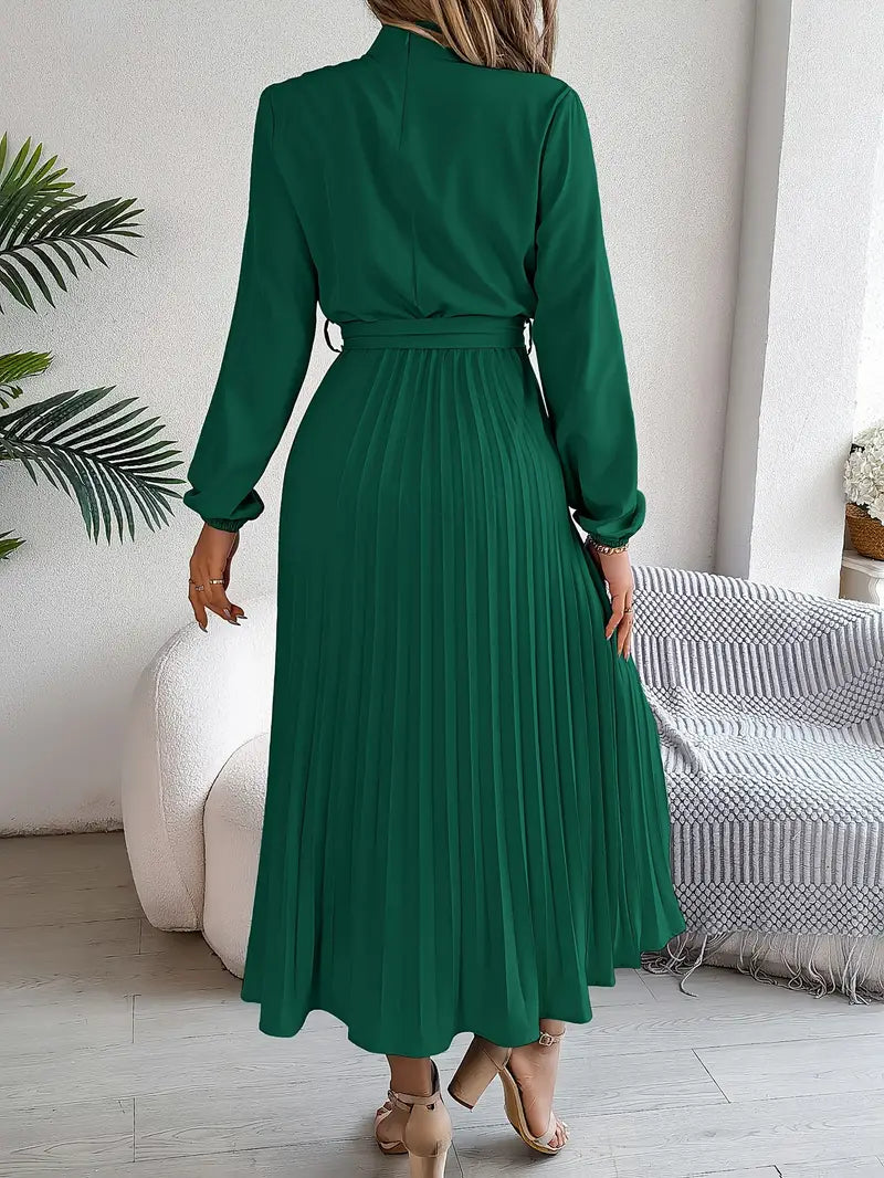 Frau in elegantem, grünem, langem Kleid mit Faltenrock, steht in modernem Wohnzimmer. Stilvolle Mode, Damenbekleidung, zeitloses Design.