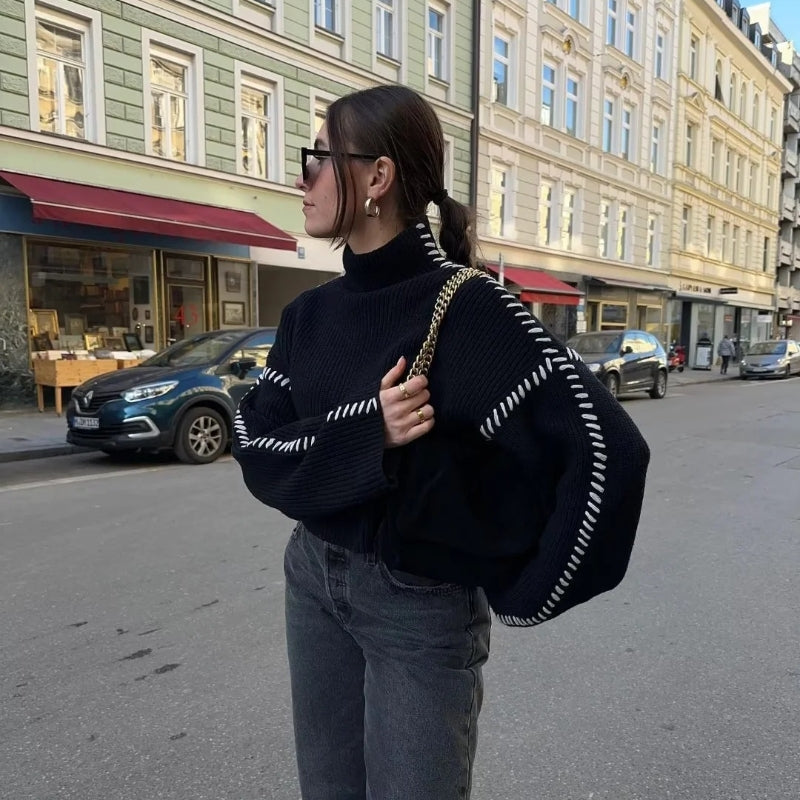 Frau in schwarzem Pullover mit weißen Nähten, grauer Jeans und Sonnenbrille auf Stadtstraße. Mode, urbaner Stil, Herbstoutfit.