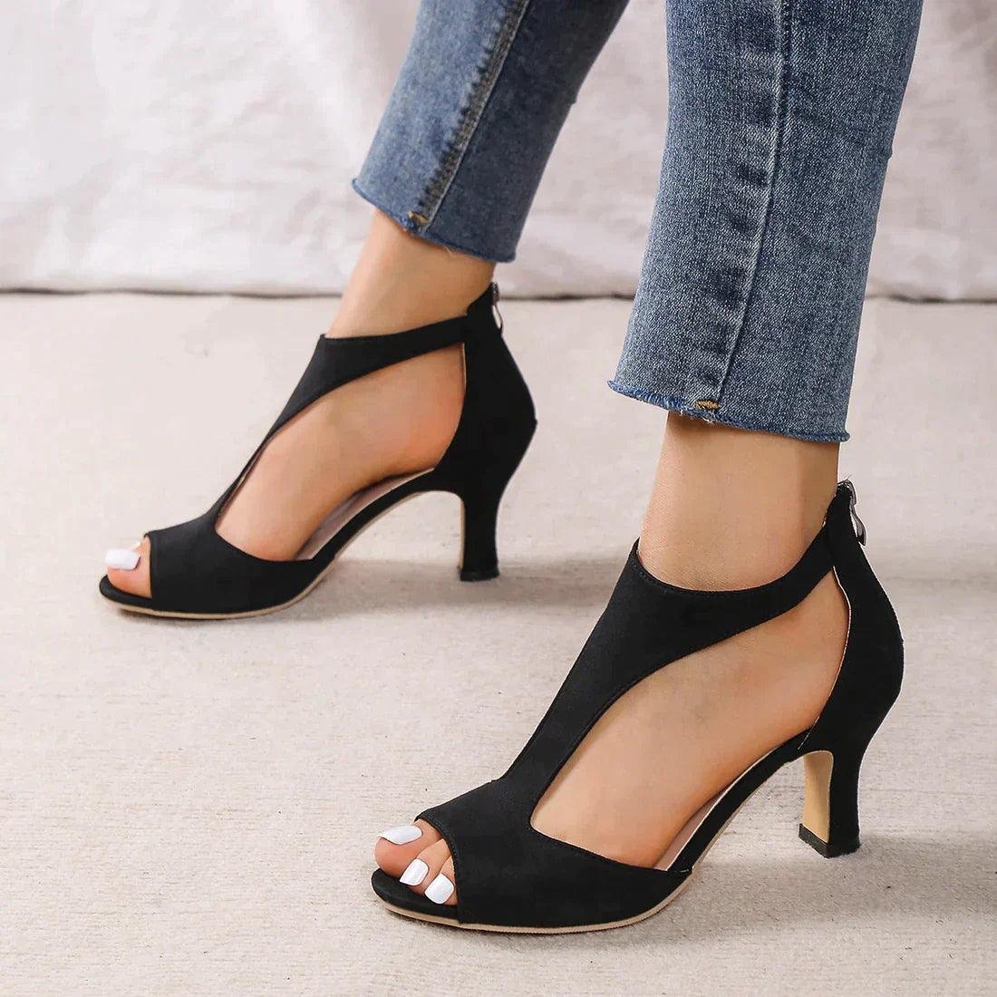 Damenfüße in eleganten schwarzen High Heels mit offenem Zeh und Jeans. Modische Schuhe, stilvoller Look, ideal für Abendveranstaltungen.