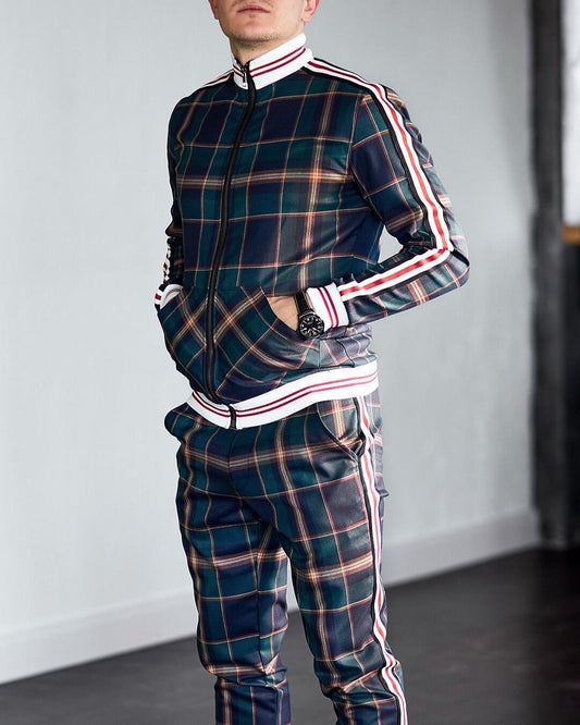 Mann in kariertem Trainingsanzug mit Reißverschluss und Streifen, steht in modernem Raum. Modetrend, Herrenbekleidung, sportlich-elegant.