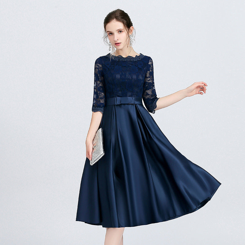 Frau in elegantem, dunkelblauem Abendkleid mit Spitzenoberteil und Dreiviertelärmeln, hält silberne Clutch. Perfekt für formelle Anlässe.