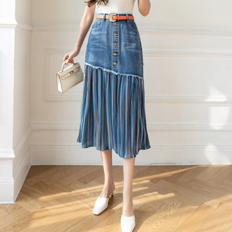 Frau in modischem Jeansrock mit Knopfleiste und Falten, trägt weiße Schuhe und eine kleine Handtasche, steht auf Holzboden vor weißer Wand.