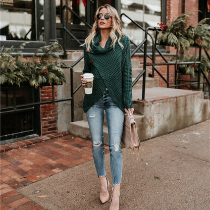 Frau in modischem, grünem Strickpullover und zerrissenen Jeans, hält Kaffeebecher, trägt Sonnenbrille, steht vor einem Café mit weihnachtlicher Dekoration.