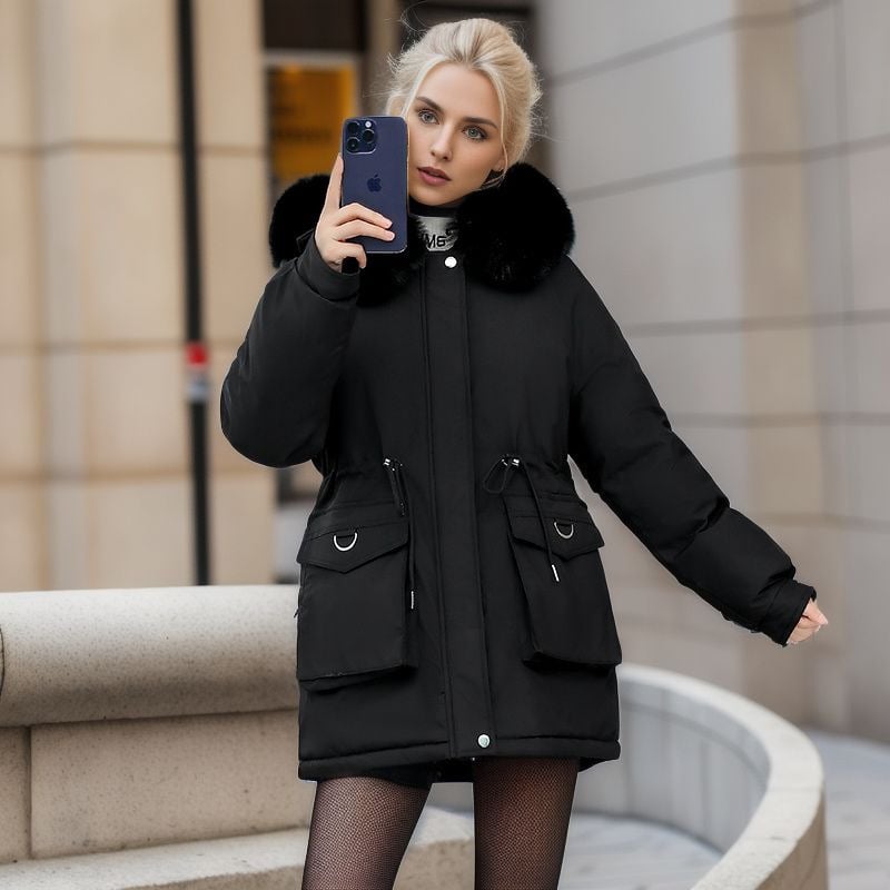 Blonde Frau in schwarzem Wintermantel mit Pelzkragen hält ein Smartphone. Stilvolle Wintermode, urbane Kulisse, moderne Technologie.