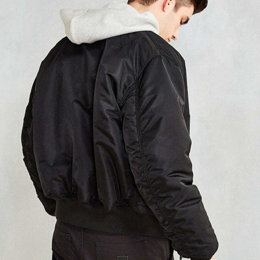 Junger Mann in schwarzer Bomberjacke und grauem Kapuzenpullover, Rückansicht. Modetrend, Streetwear, lässiger Stil, Herbstmode.