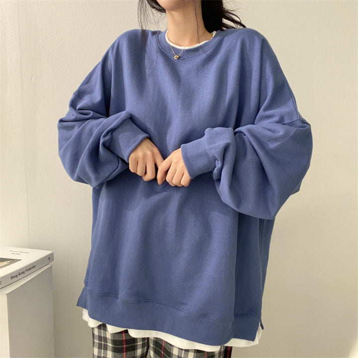 Frau in blauem Oversize-Pullover, kombiniert mit karierten Hosen, steht vor weißer Wand. Modetrend, lässiger Stil, bequeme Kleidung.