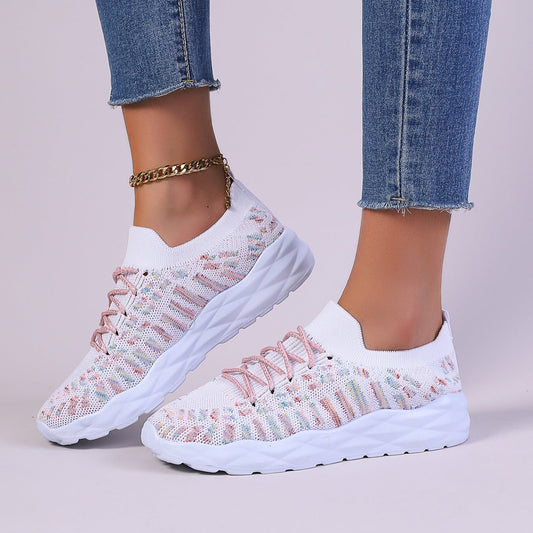 Damen Sneaker in Weiß mit rosa Details, gestricktes Obermaterial, dicke Sohle, kombiniert mit blauer Jeans und goldener Fußkette.