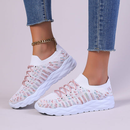 Damen Sneaker in Weiß mit rosa Details, gestricktes Obermaterial, dicke Sohle, kombiniert mit blauer Jeans und goldener Fußkette.