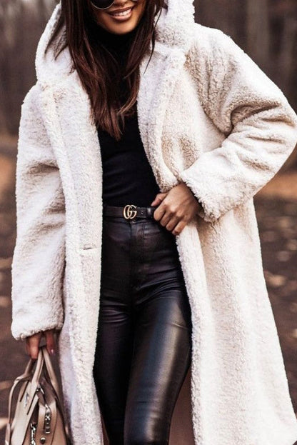 Frau in weißem Teddy-Mantel, schwarzem Rollkragenpullover und Lederhose, hält eine Handtasche. Herbstmode, stilvoll, elegant, Outdoor.