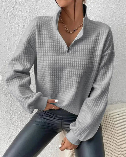 Frau in grauem, gestepptem Pullover mit Reißverschluss und Kette, trägt schwarze Lederleggings. Modetrend, Herbstmode, Damenbekleidung.