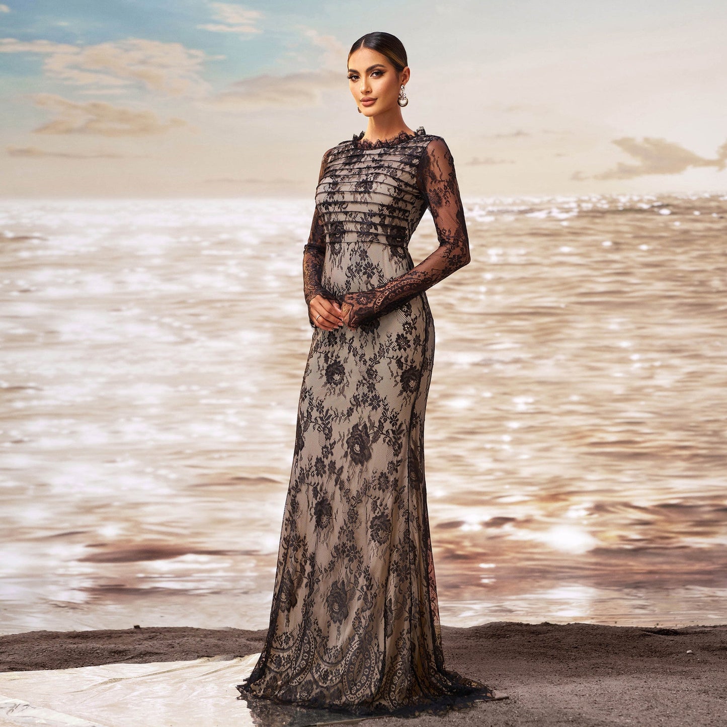 Frau in eleganter Abendkleidung am Strand, schwarzes Spitzenkleid, Sonnenuntergang im Hintergrund, glamouröses Modefoto, stilvolle Abendmode.