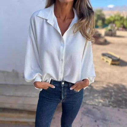 Frau in weißer Bluse und blauer Jeans, lässig stehend mit Händen in den Taschen, draußen bei sonnigem Wetter. Mode, Freizeitkleidung, Damenoutfit.