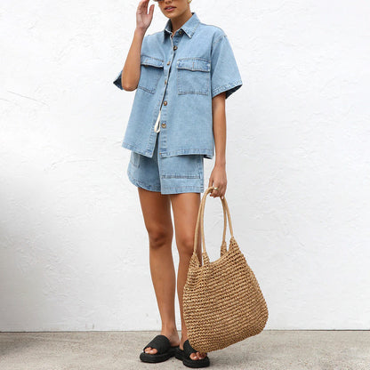 Frau in lässigem Jeans-Shorts-Set mit Strohtasche und schwarzen Sandalen vor weißer Wand. Sommermode, Denim-Outfit, Freizeitlook.