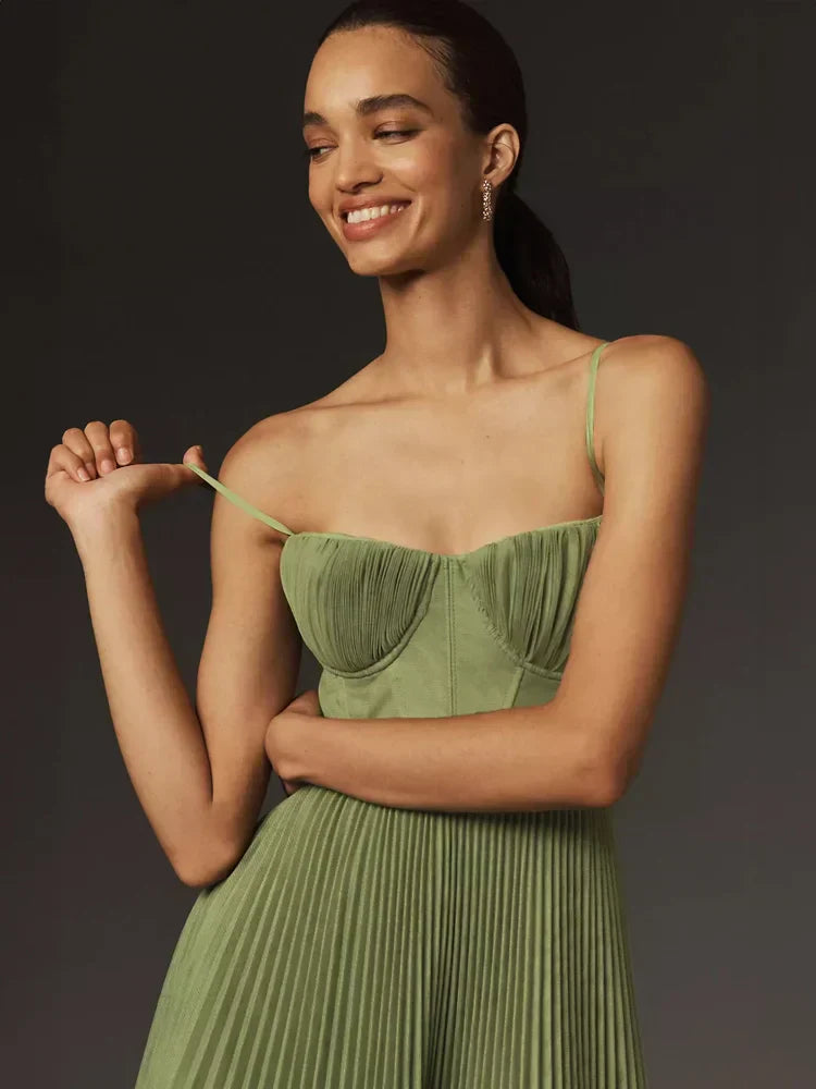 Frau in grünem, plissiertem Kleid mit Spaghettiträgern, lächelnd vor dunklem Hintergrund. Elegantes Abendkleid, Mode, Damenbekleidung.