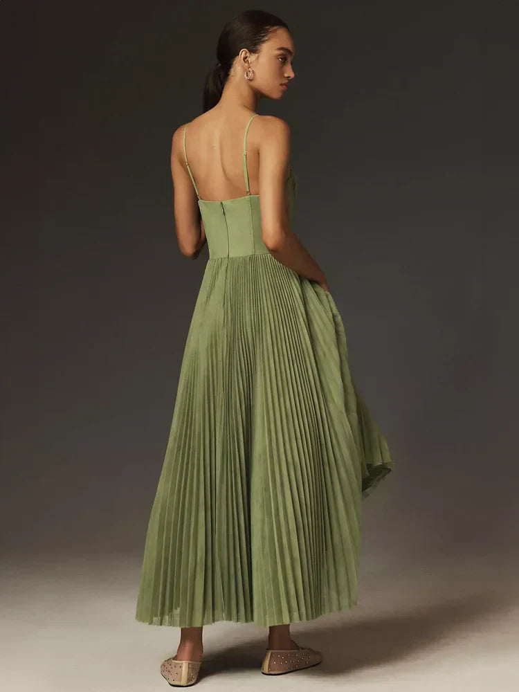 Frau in langem, grünem, plissiertem Kleid mit Spaghettiträgern, seitlich stehend, elegantes Abendoutfit, modische Damenmode, stilvolle Kleidung.