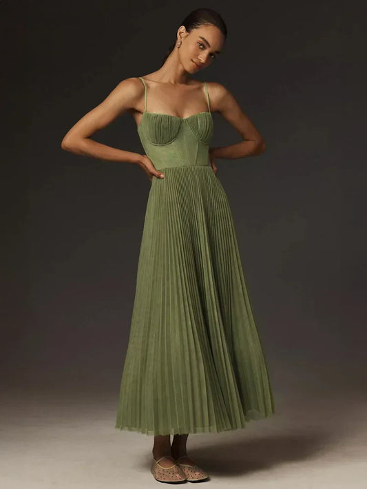 Frau in elegantem, grünem, plissiertem Abendkleid mit Spaghettiträgern, posiert vor dunklem Hintergrund. Mode, Abendkleid, Damenmode, Eleganz.