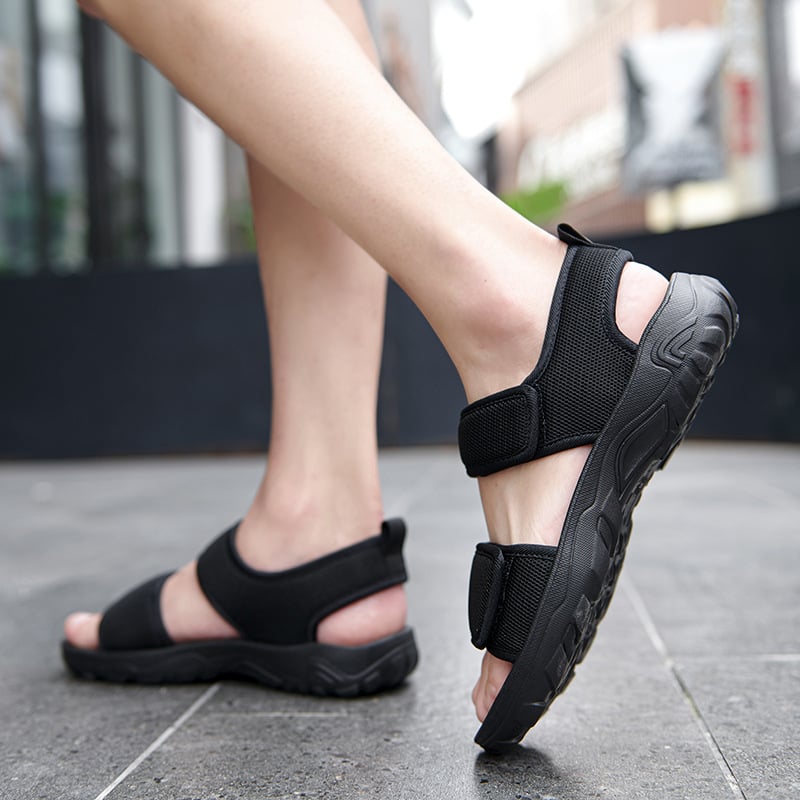 Schwarze Outdoor-Sandalen an Füßen auf Gehweg, ideal für Sommer, Wandern und Freizeit. Bequeme, rutschfeste Schuhe für Damen und Herren.