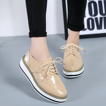 Beige Damen-Brogues mit Plateau, glänzendem Finish und Schnürung, getragen von Person in schwarzer Hose. Modische Schuhe, trendiger Look.