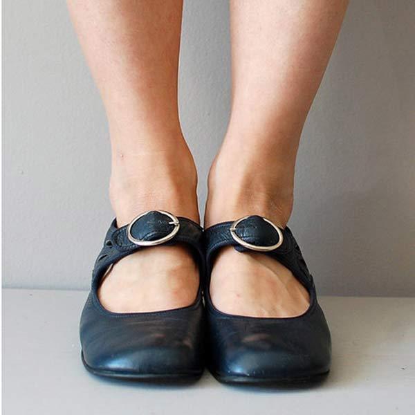 Schwarze Mary Jane Schuhe mit Schnallen an Frauenfüßen, stehend auf grauem Boden. Bequeme Damenschuhe, klassisches Design, modisch und zeitlos.