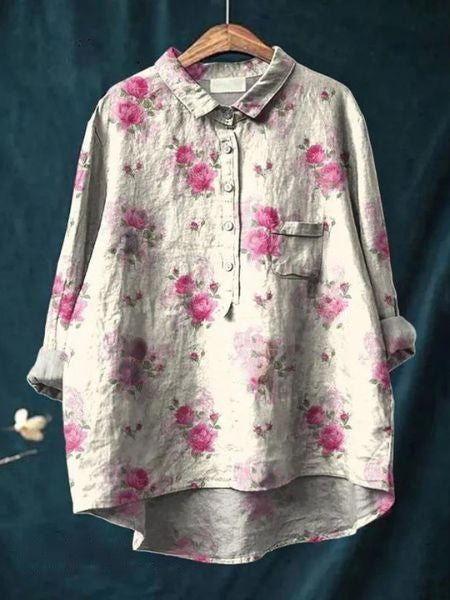 Graues Leinenhemd mit rosa Blumenmuster, Knopfleiste und Brusttasche, hängend auf einem Holzkleiderbügel vor dunkelblauem Hintergrund.
