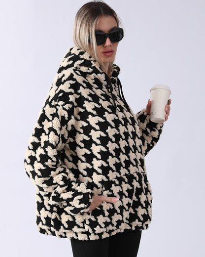 Frau in schwarz-weißem Hahnentritt-Fleece-Hoodie, hält Kaffeebecher, trägt Sonnenbrille. Modetrend, Wintermode, lässiger Stil.