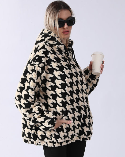 Frau in schwarz-weißem Hahnentritt-Fleece-Hoodie, hält Kaffeebecher, trägt Sonnenbrille. Modetrend, Wintermode, lässiger Stil.