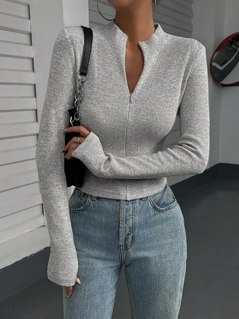 Frau in grauem, langärmligem Oberteil und blauer Jeans, hält schwarze Handtasche. Modetrend, lässiger Look, stilvolle Damenbekleidung.
