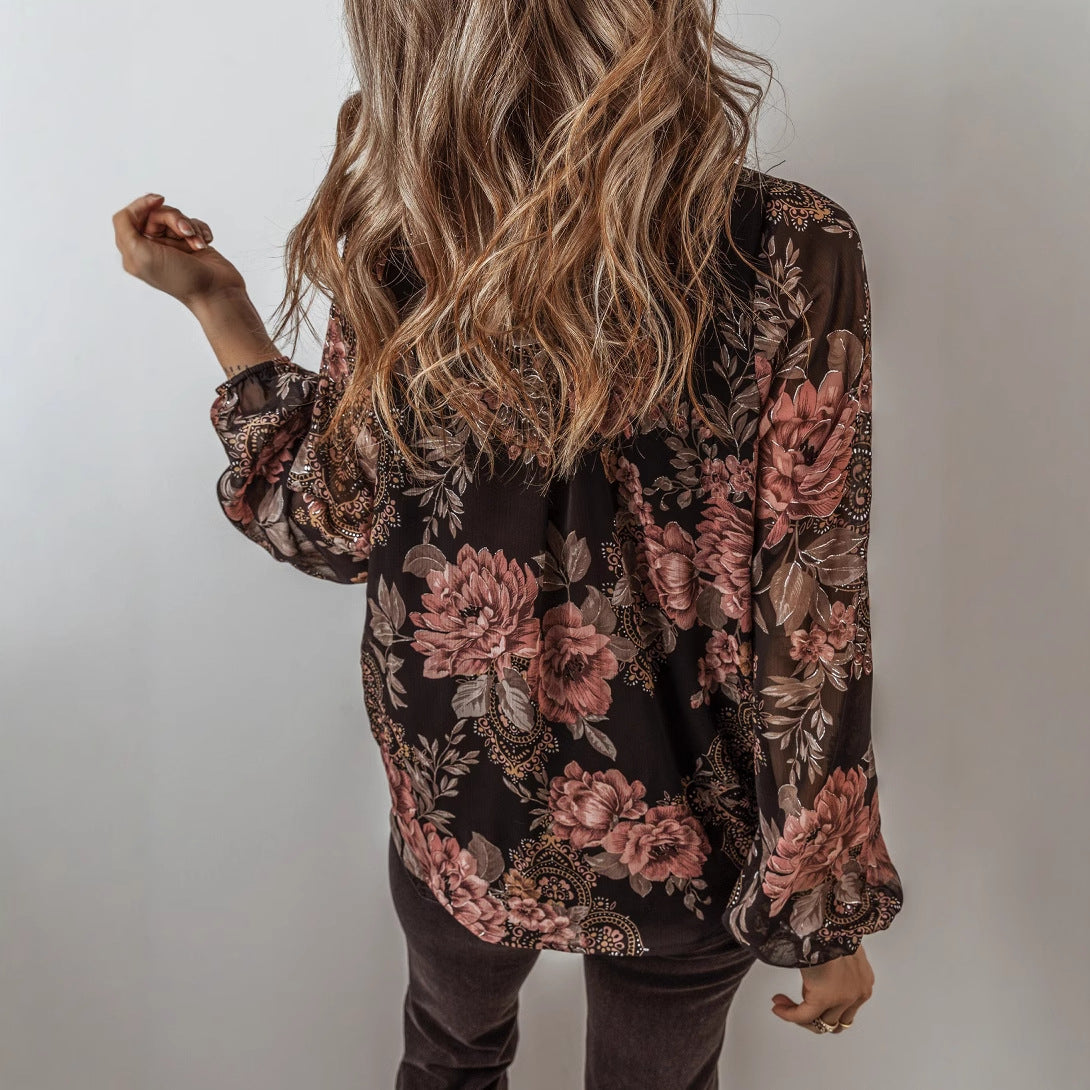 Frau mit langen, welligen Haaren trägt eine schwarze Bluse mit rosa Blumenmuster. Modetrend, Damenmode, florales Design, Herbstoutfit.