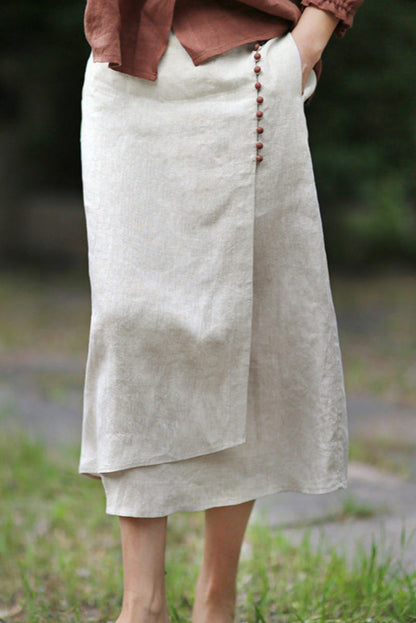 Beiger Leinenrock mit asymmetrischem Schnitt und seitlichen Knöpfen, getragen von einer Person im Freien. Elegante Damenmode, Sommeroutfit.