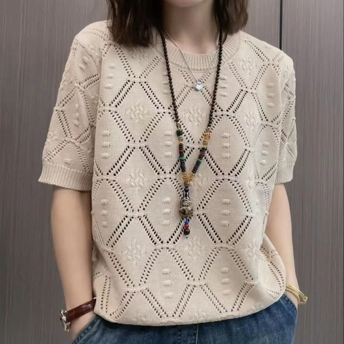 Dame in beigem Strickpullover mit geometrischem Muster, trägt lange Halskette. Modetrend, Strickmode, Damenbekleidung, lässiger Stil.