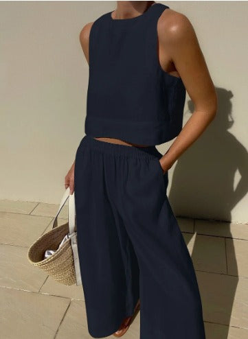 Dame in dunkelblauem ärmellosen Top und weiter Hose, hält eine Strohtasche. Sommermode, lässiger Stil, elegantes Outfit, minimalistisch.