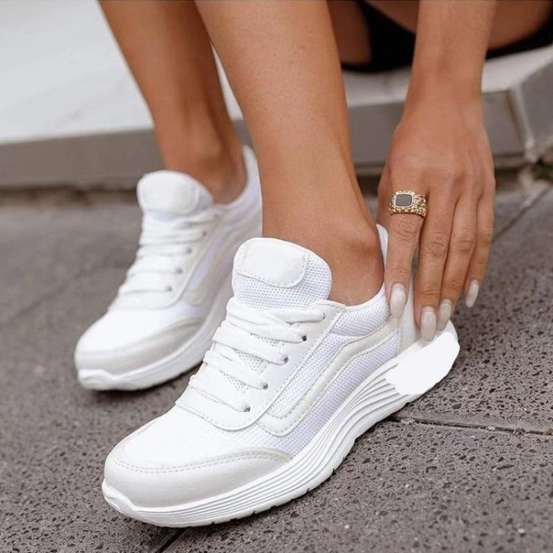 Weiße Damen-Sneaker mit dicker Sohle, getragen von einer Person auf grauem Pflaster. Moderne Sportschuhe, ideal für Freizeit und Sport.