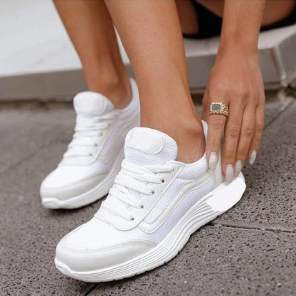 Weiße Damen-Sneaker mit dicker Sohle, getragen von einer Person auf grauem Pflaster. Moderne Sportschuhe, ideal für Freizeit und Sport.
