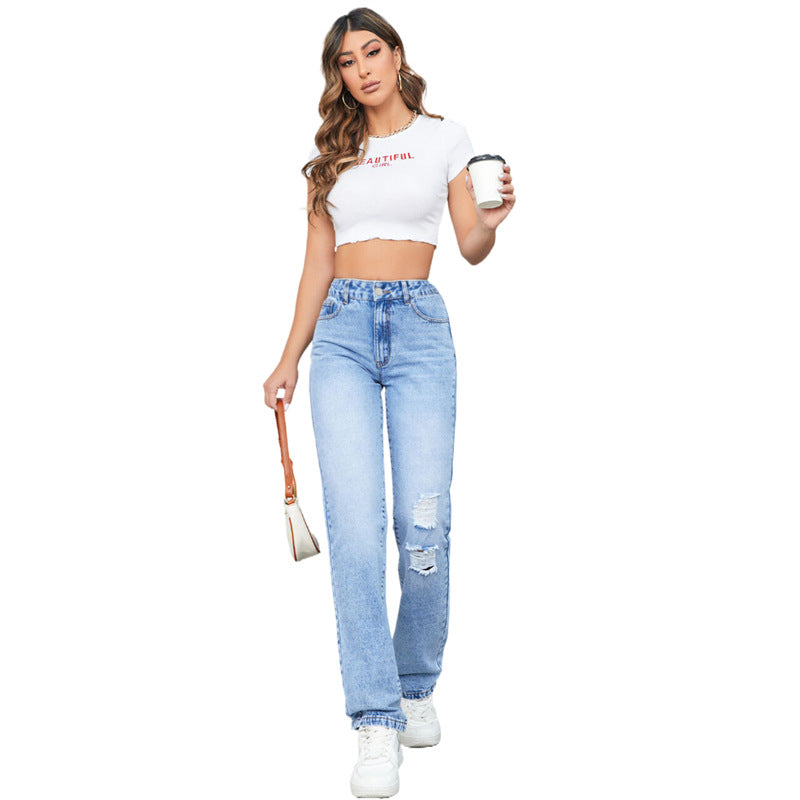 Junge Frau in zerrissenen Jeans und weißem Crop-Top, hält Kaffeebecher und Handtasche. Modetrend, Freizeitlook, Streetstyle.