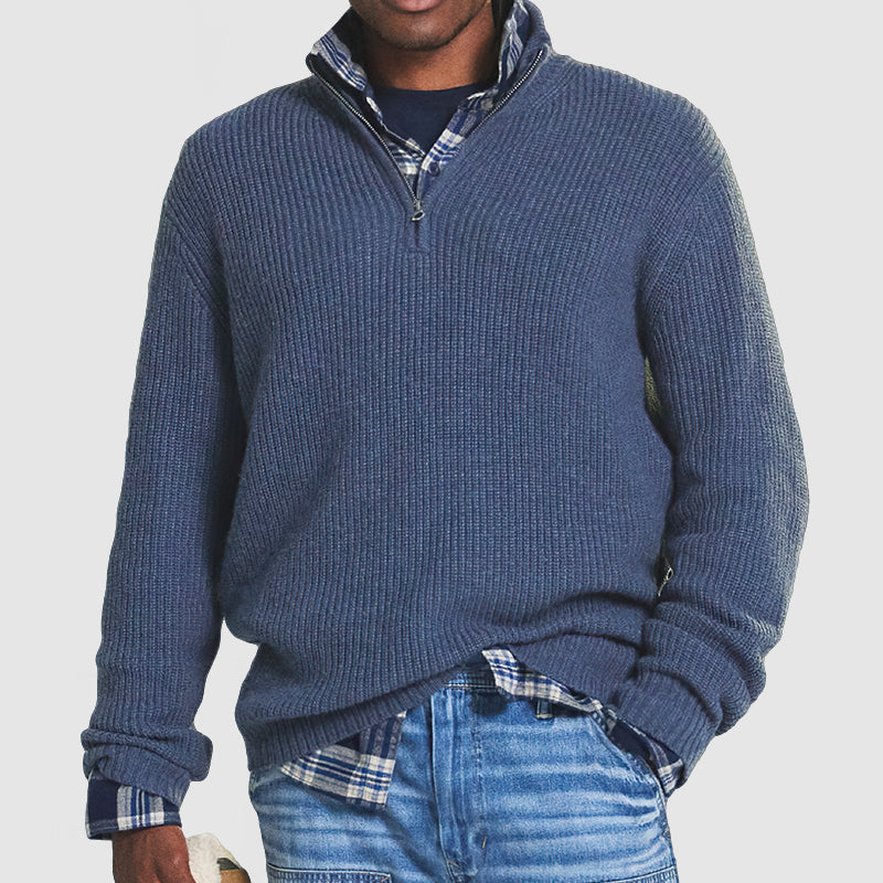 Mann in blauem Strickpullover mit Reißverschluss, kariertem Hemd und Jeans. Modischer Freizeitlook für Herren.