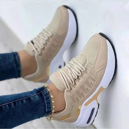 Beige Sneaker mit weißer Sohle, goldenen Akzenten und Schnürsenkeln, getragen von Person in blauer Jeans. Modische Damen-Sportschuhe.