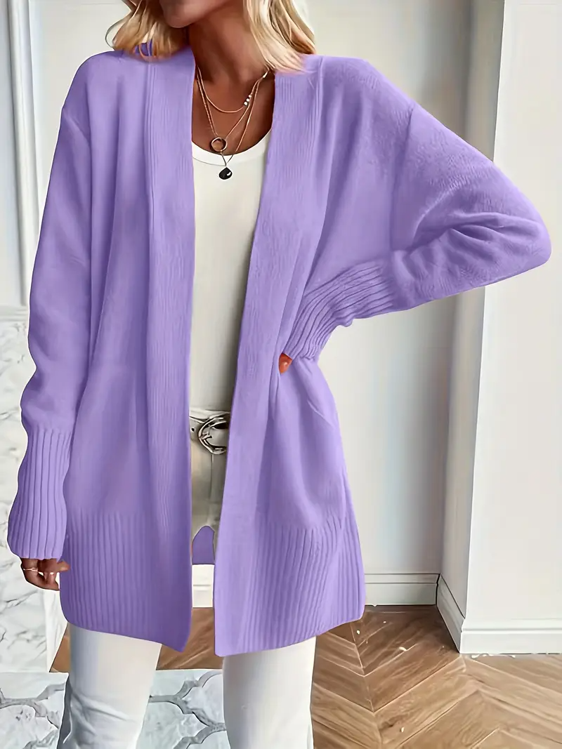 Frau trägt lila Strickjacke über weißem Top und Hose, modisch, lässig, Herbstmode, Damenbekleidung, eleganter Look, Innenaufnahme.