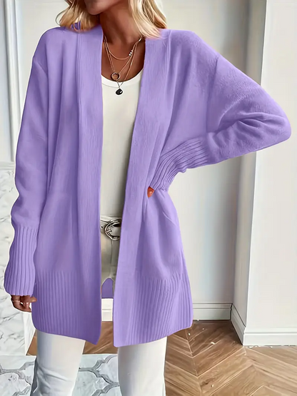 Frau trägt lila Strickjacke über weißem Top und Hose, modisch, lässig, Herbstmode, Damenbekleidung, eleganter Look, Innenaufnahme.