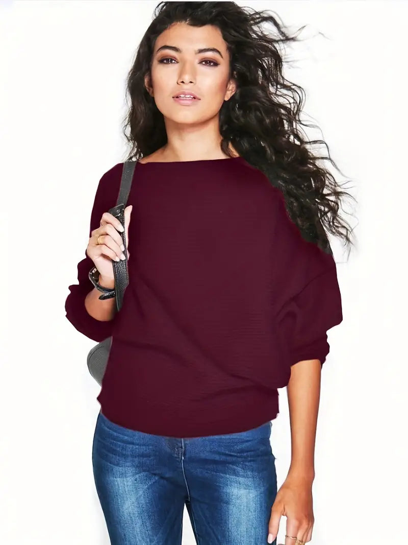 Eine Frau in einem weinroten Pullover und blauen Jeans, mit welligem Haar, posiert vor einem weißen Hintergrund. Mode, Damenbekleidung, lässiger Stil.