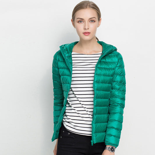 Frau in grüner Daunenjacke mit Kapuze, gestreiftem Shirt und schwarzer Hose vor weißem Hintergrund. Modetrend, Winterjacke, Damenbekleidung.