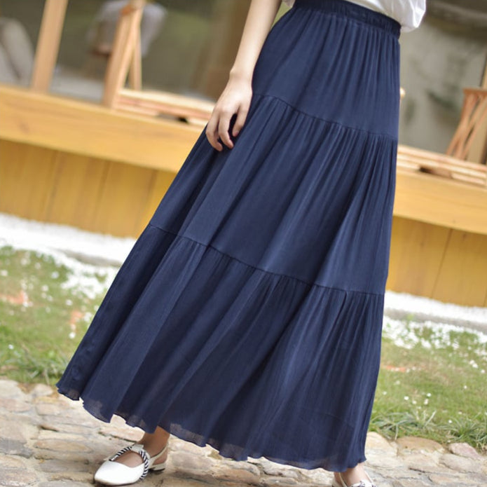 Frau in langem, dunkelblauem Maxirock aus leichtem Stoff, steht auf einem gepflasterten Weg. Sommermode, eleganter Stil, Freizeitkleidung.