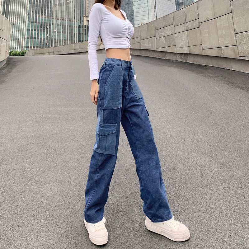 Frau in weißem Crop-Top und blauer Cargo-Jeans posiert auf städtischer Straße. Modetrend, lässiger Stil, urbane Mode, Streetwear-Look.