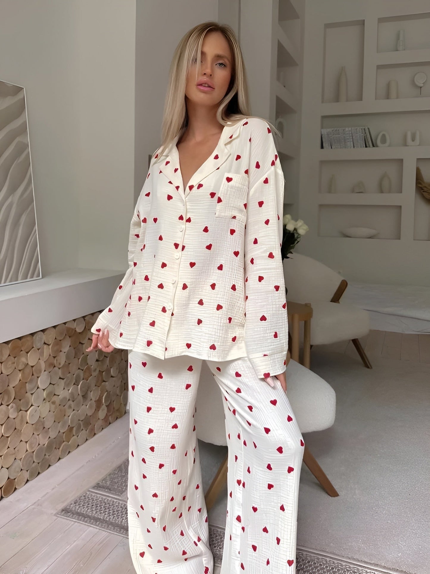 Frau in weißem Pyjama mit roten Herzen, steht in modernem Wohnzimmer. Gemütliche Nachtwäsche, stilvolle Inneneinrichtung, entspannte Atmosphäre.