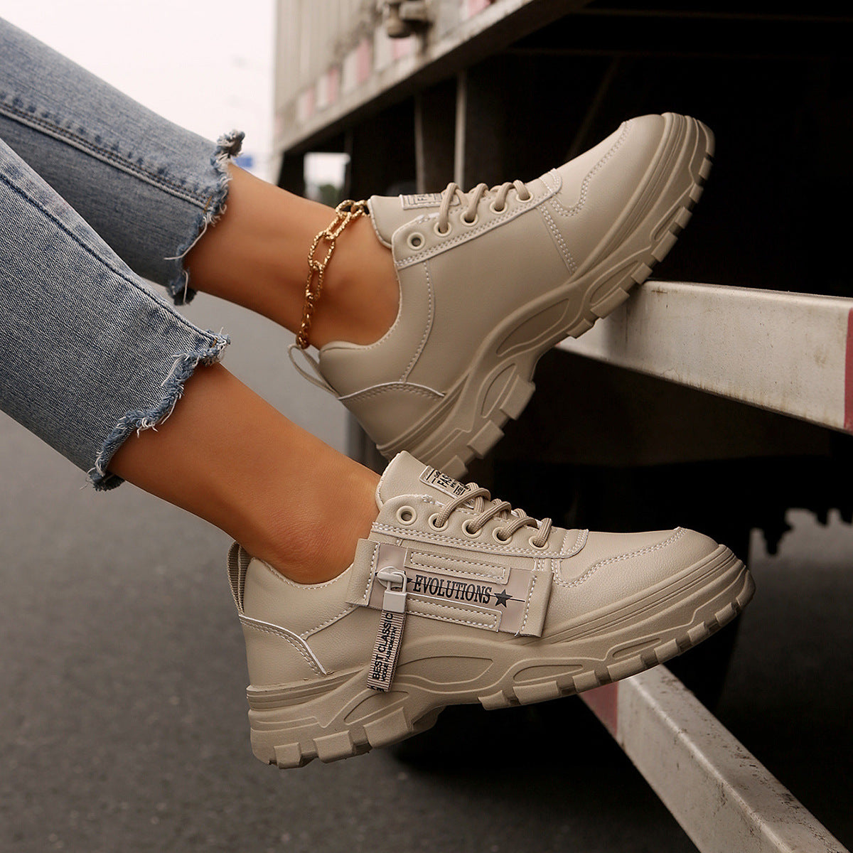 Beige Sneaker mit dicker Sohle, getragen von Person in Jeans, nahe LKW. Modische Damen-Schuhe, urbaner Stil, ideal für Freizeit und Streetwear.