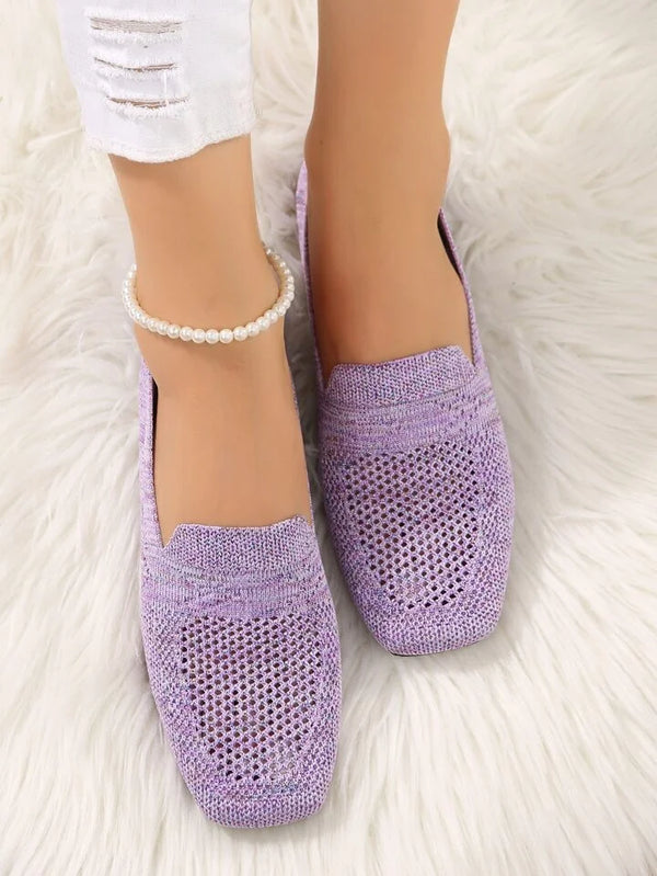 Lila gestrickte Damen-Loafer auf weißem Teppich, kombiniert mit zerrissenen weißen Jeans und Perlenknöchelband. Bequeme, modische Schuhe.
